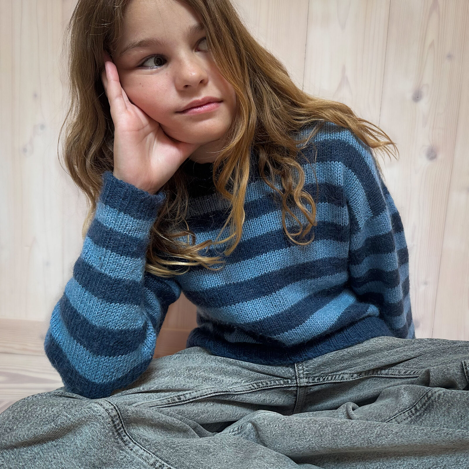 Jente i blåstripet strikkegenser sitter og hviler hodet i hånden